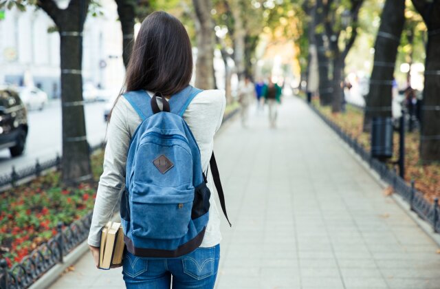 A behind view of a female student walking with a backpack on and holding books.
