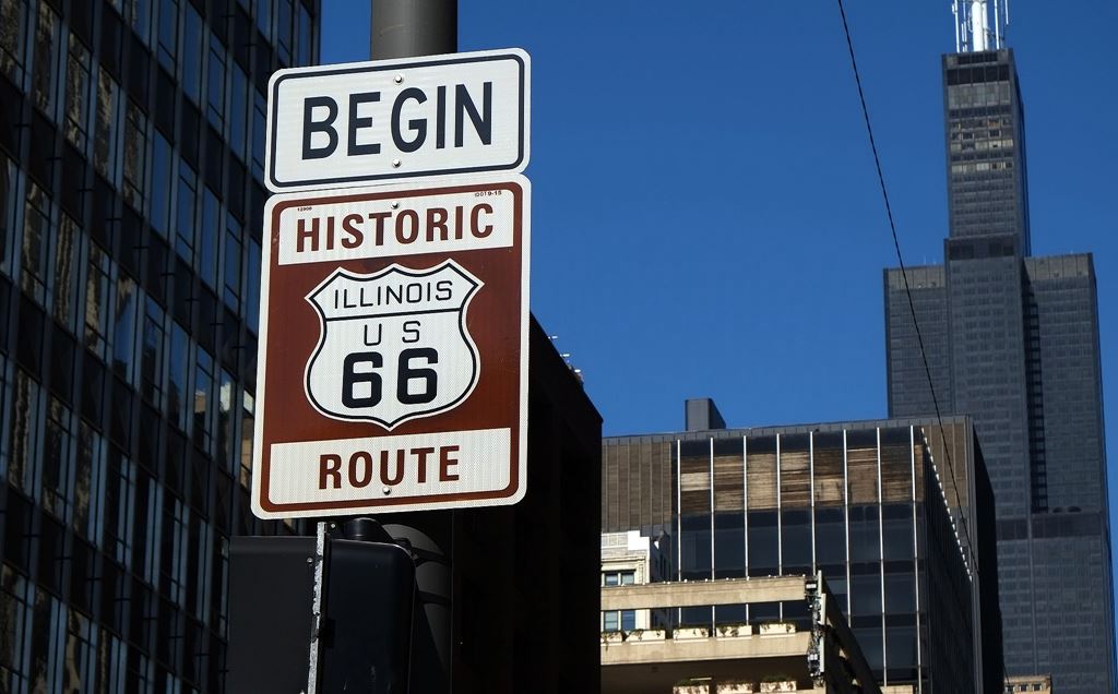 Sign that says Begin Historic Illinois US Route 66 in front of city buildings.