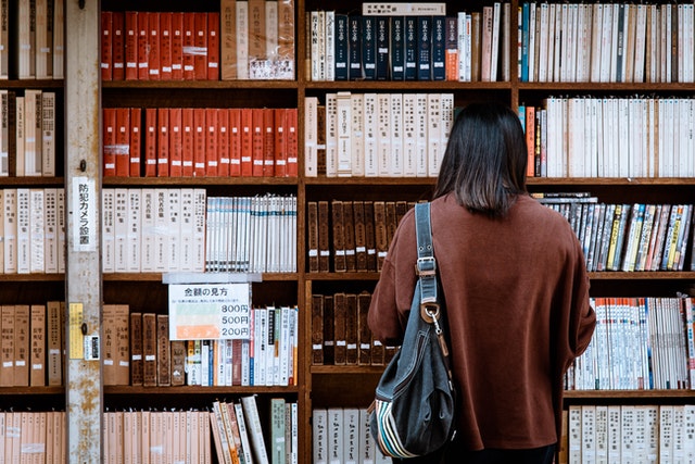 A woman faces a shelf of books.