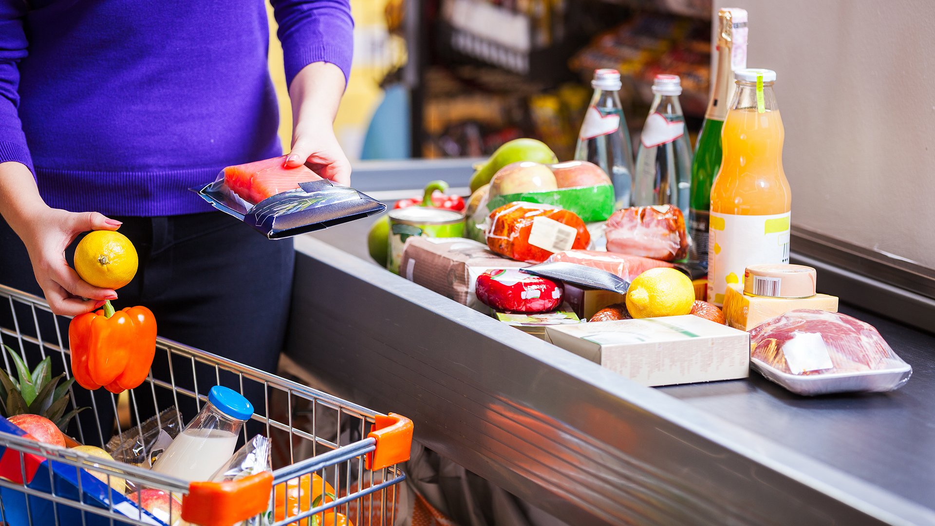 A person grabs food items from a cart and places them on a checkout belt.