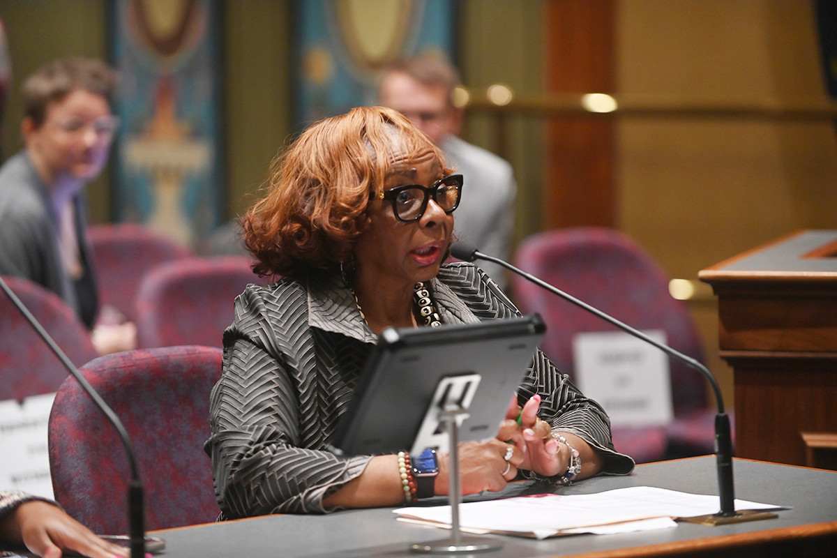 Senator Hunter speaks into a microphone while seated at a table during a committee hearing.